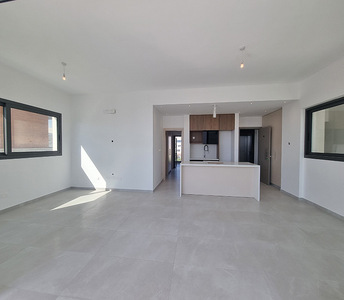 Open-plan living area of the flat with large-format tiles, minimalist kitchen with wood accents, and dual-aspect windows