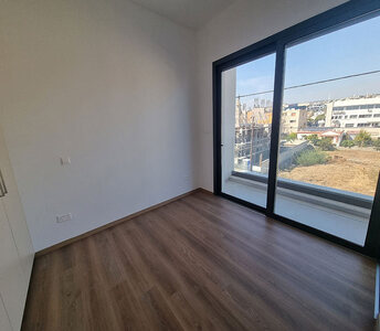 The second bedroom of the apartment with wood-style flooring, large sliding glass doors, and urban views